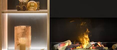 Una chimenea moderna con encierro de vidrio, objetos decorativos en estantes y fuego encendido.