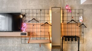 Habitación de hotel moderna con una pared de cuadrícula, un letrero de neón con forma de flamenco, un espejo y un perchero negro.