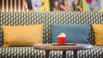 A cozy seating area with a patterned sofa, a round table, and a red mug with whipped cream.
