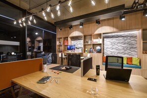 A modern office space with a wooden desk, a laptop, and various office supplies. There are cubicles, a sofa with cushions, and a decorative wall with a textured pattern.