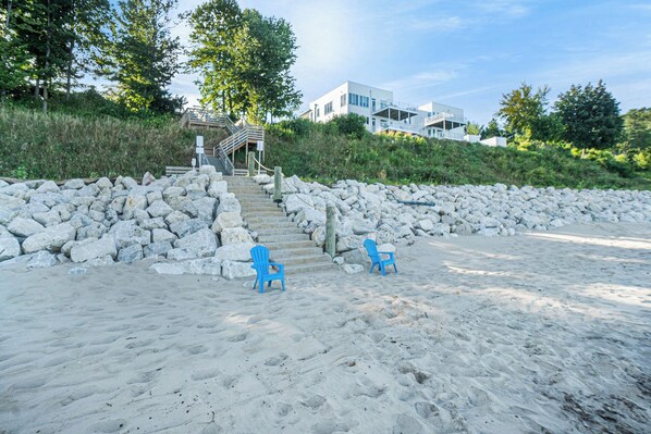 A beach with two blue chairs, a stone wall, and a staircase leading to a building. - 🏖️Sleepy Hollow Beach Resort, Stonebridge 37 – Family Fun on Lake Michigan! (South Haven)