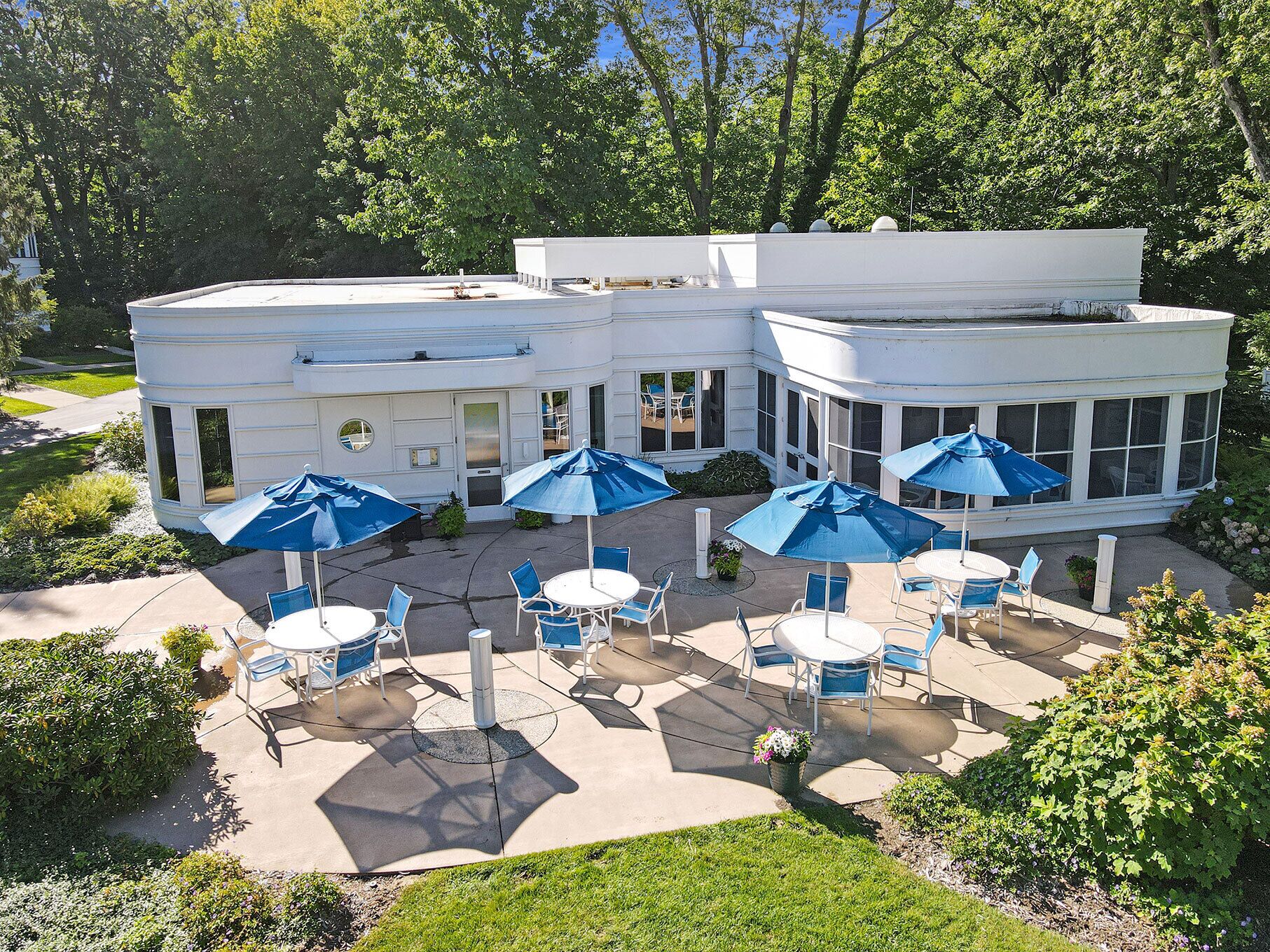 Een wit gebouw met een patio, voorzien van zitplaatsen buiten en blauwe parasols.