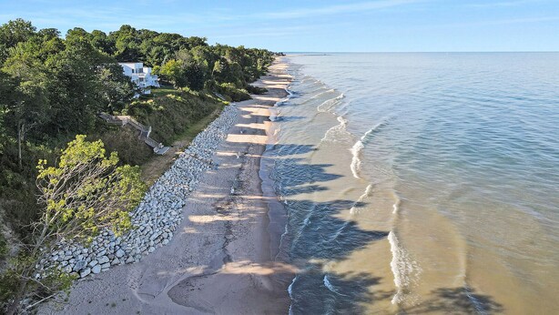 A coastal property with a paved walkway along the beach, a stone wall, and a house with a view of the sea.