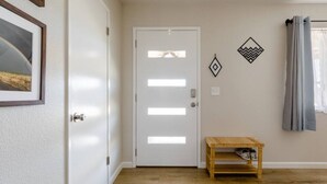 A hallway with a white door, a small wooden bench, and two wall decorations. - The Desert Peacock, Hot Tub, Central AC & VIEWS (Yucca Valley)