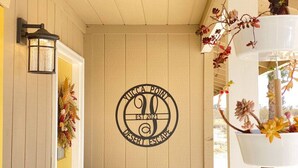A wooden door with a circular logo and a hanging planter with flowers. - The Desert Peacock, Hot Tub, Central AC & VIEWS (Yucca Valley)