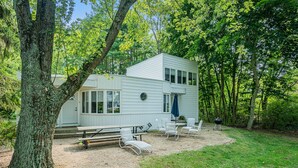 A modern two-story cabin with a patio area, surrounded by trees.