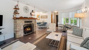 A living room with a stone fireplace, a dining area with a table and chairs, and a sofa with a patterned pillow.