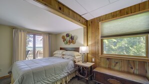 A bedroom with a large bed, a wooden bench, a lamp, and a window with a view of trees. - 21 Mi to Slopes! Torch Lake Home w/ Private Beach (Rapid City)