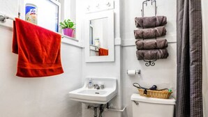 A bathroom with a white sink, a red towel, a mirror, and a toilet with a basket on it.