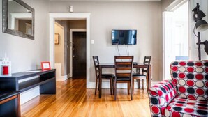A living room with a wooden floor, a black TV stand, a red-framed picture, and a patterned sofa.