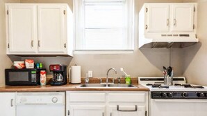 A compact kitchen with white cabinets, a microwave, a coffee maker, a sink, and a stove.
