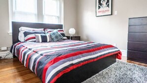 A bedroom with a bed, a gray rug, a nightstand, a lamp, and a framed picture on the wall.