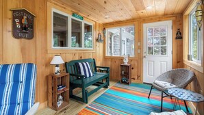 L’intérieur chaleureux d’un chalet, avec un décor en bois, un canapé vert, un tapis à rayures et un fauteuil près de la fenêtre.