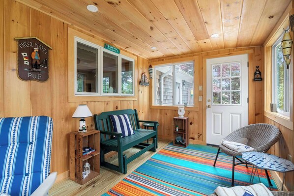 Interior acogedor de una cabaña con detalles de madera, un sofá verde, una alfombra a rayas y un sillón junto a la ventana.