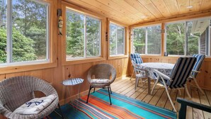 A wooden deck with wicker chairs and a table, large windows, and a view of trees. - Easy Bike Path Access, Dog Welcome! (Chatham)
