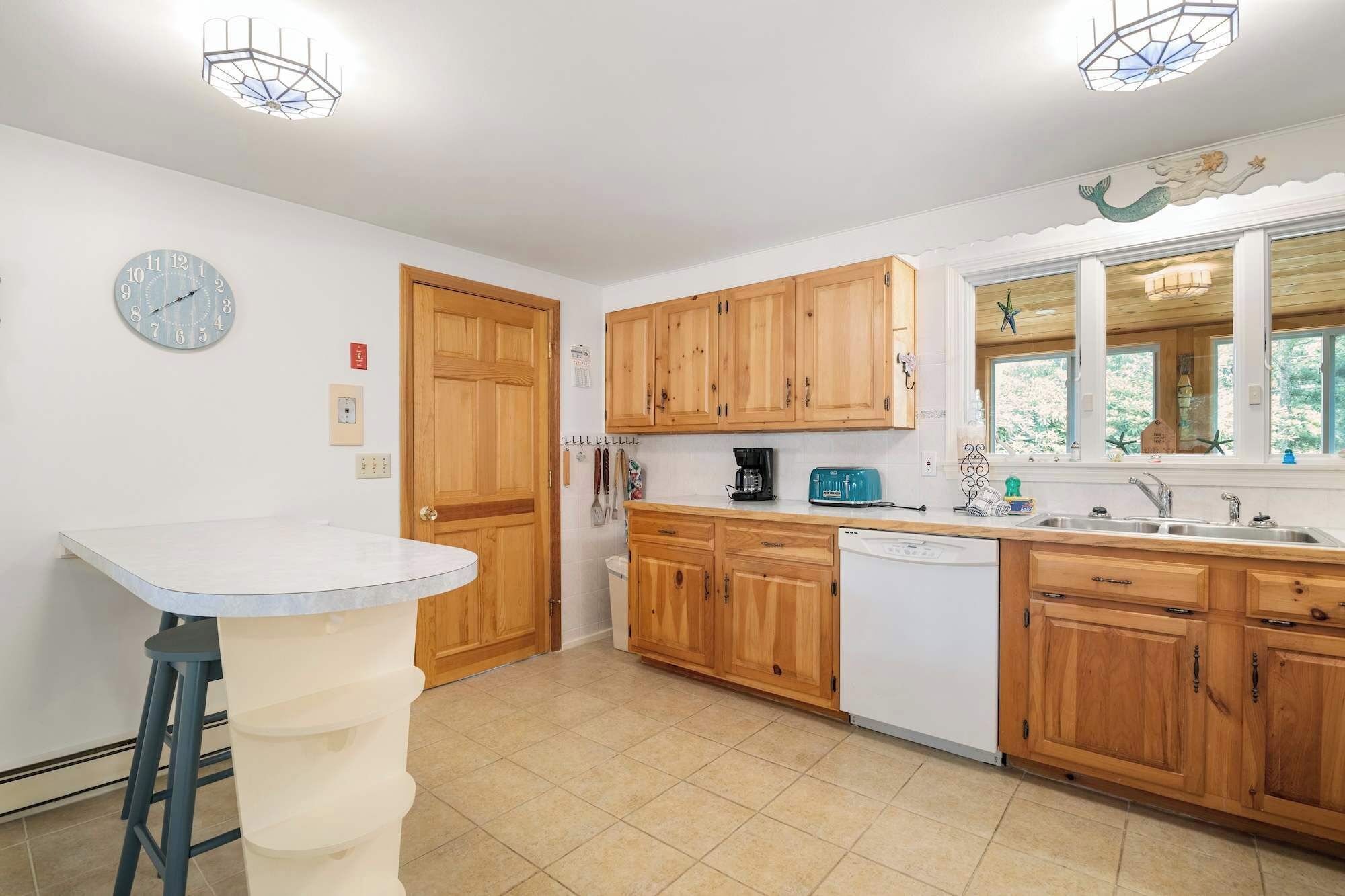 A kitchen with wooden cabinets, a white countertop, a clock, and a window with a view.