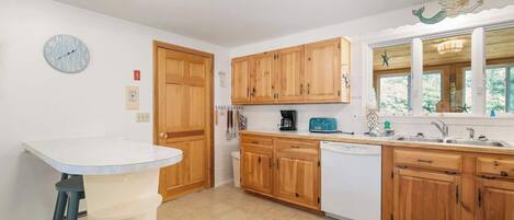 A kitchen with wooden cabinets, a white countertop, a clock, and a window with a view.