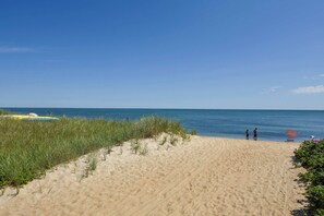 Une plage de sable fin, un ciel bleu dégagé, quelques personnes et un parasol de plage.