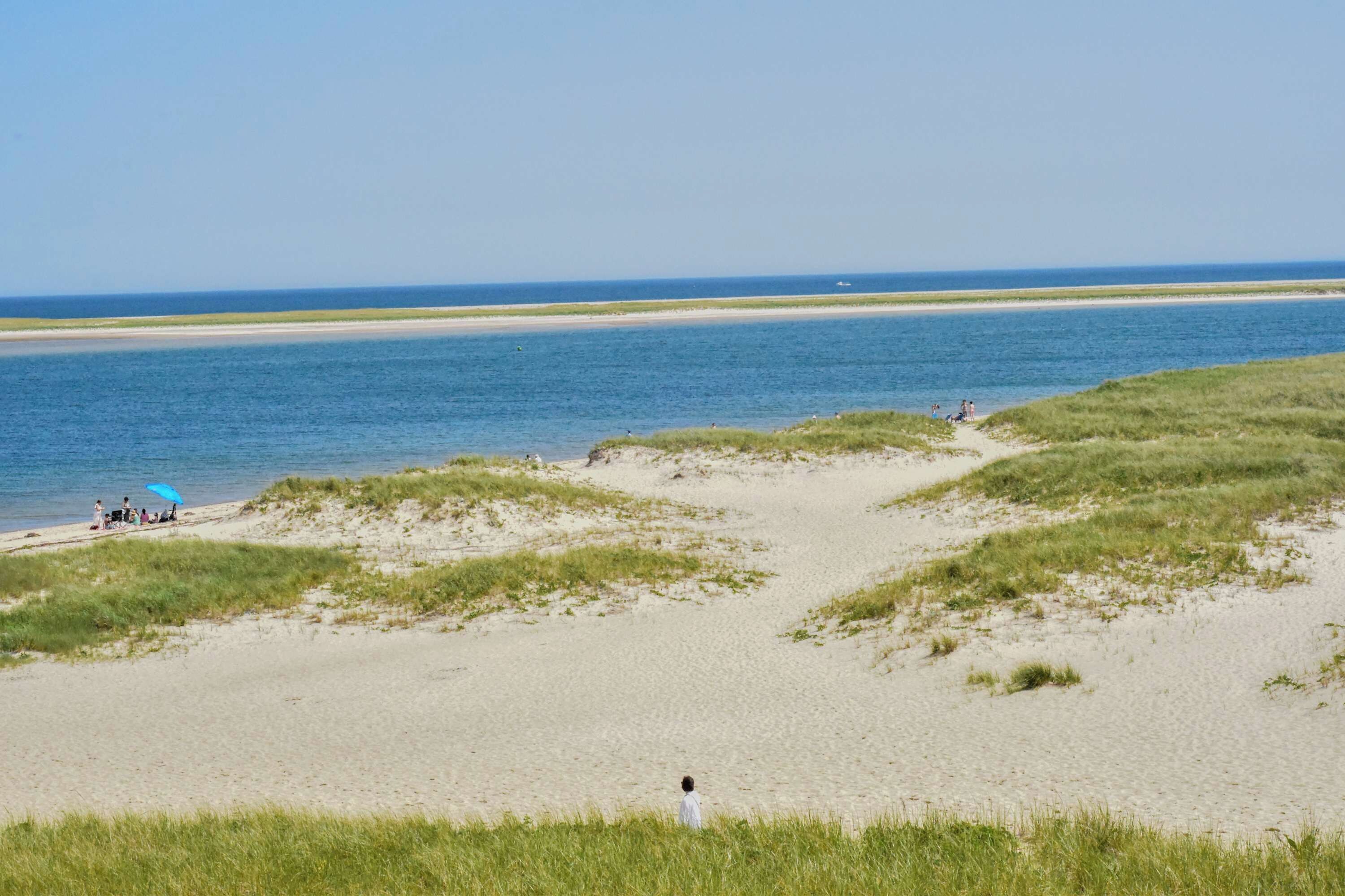 Een strand met heldere lucht, zandduinen en een rustige zee.