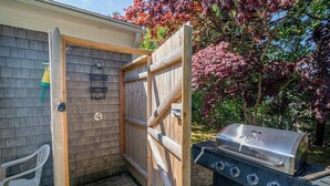 A wooden outdoor grill and a wooden gate leading to a covered area with a hose and a chair. - Easy Bike Path Access, Dog Welcome! (Chatham)