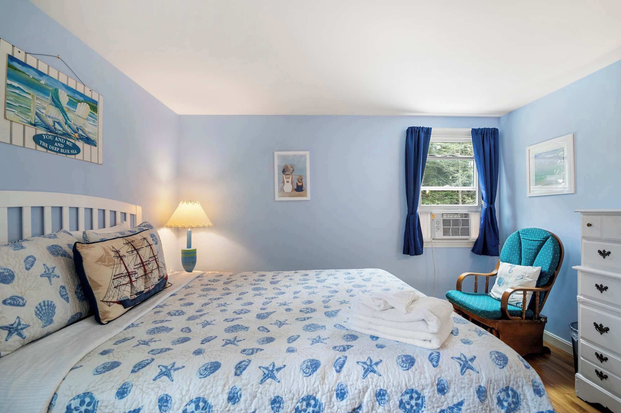A bedroom with a bed, a chair, a dresser, and a window with curtains.