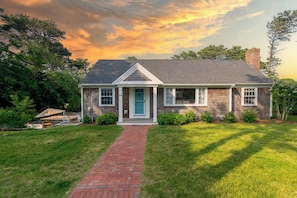 A two-story house with a brick pathway leading to the front door, surrounded by greenery.