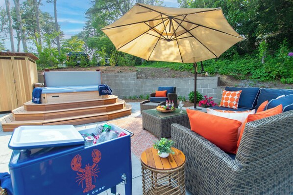 An outdoor patio with a hot tub, wicker furniture, and a large umbrella.