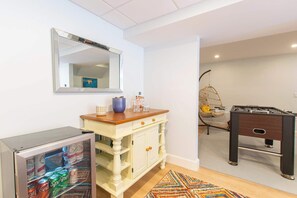A room with a minibar, a white cabinet, a foosball table, and a hanging chair.