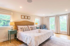 A bedroom with a large bed, two bedside tables, a chair, and a window with curtains.
