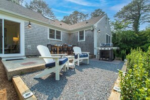 A house with a patio area featuring Adirondack chairs, a grill, and a dining table.