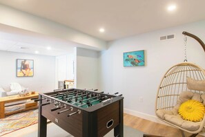 A modern living room with a foosball table, a hanging chair, and artwork on the walls.