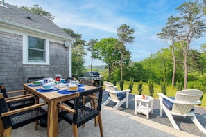 Eine Terrasse im Freien mit Esstisch, umgeben von Adirondack-Stühlen und einem Grill.