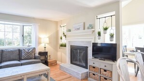 A living room with a fireplace, sofa, television, and dining area. - Beautiful Home Close to Ponds and Beach! (Brewster)