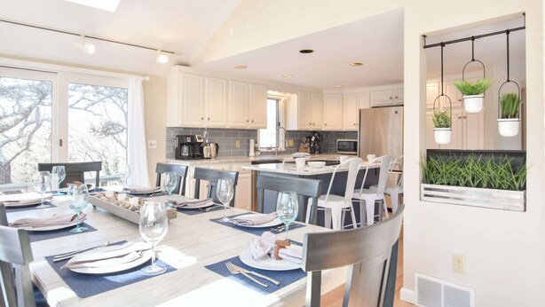 A modern kitchen with white cabinets, a central island, and hanging plants. - Beautiful Home Close to Ponds and Beach! (Brewster)