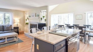 A modern kitchen with a central island, built-in oven, and dining area with a table and chairs. - Beautiful Home Close to Ponds and Beach! (Brewster)