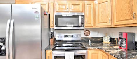 A kitchen with wooden cabinets, a stainless steel refrigerator, a microwave, an oven, and a coffee maker.