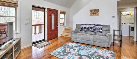 A spacious living room with hardwood floors, a gray sofa, a wooden entertainment unit, and a large floral rug.