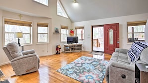A spacious living room with a large window, a television, and a cozy fireplace. - Cozy Hayesville Retreat w/ Deck & Mtn Views! (Hayesville)