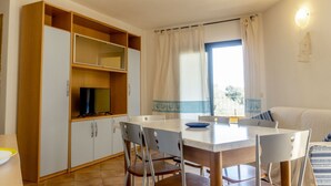 Un espacio habitable compacto con comedor, televisor y ventana con cortinas.