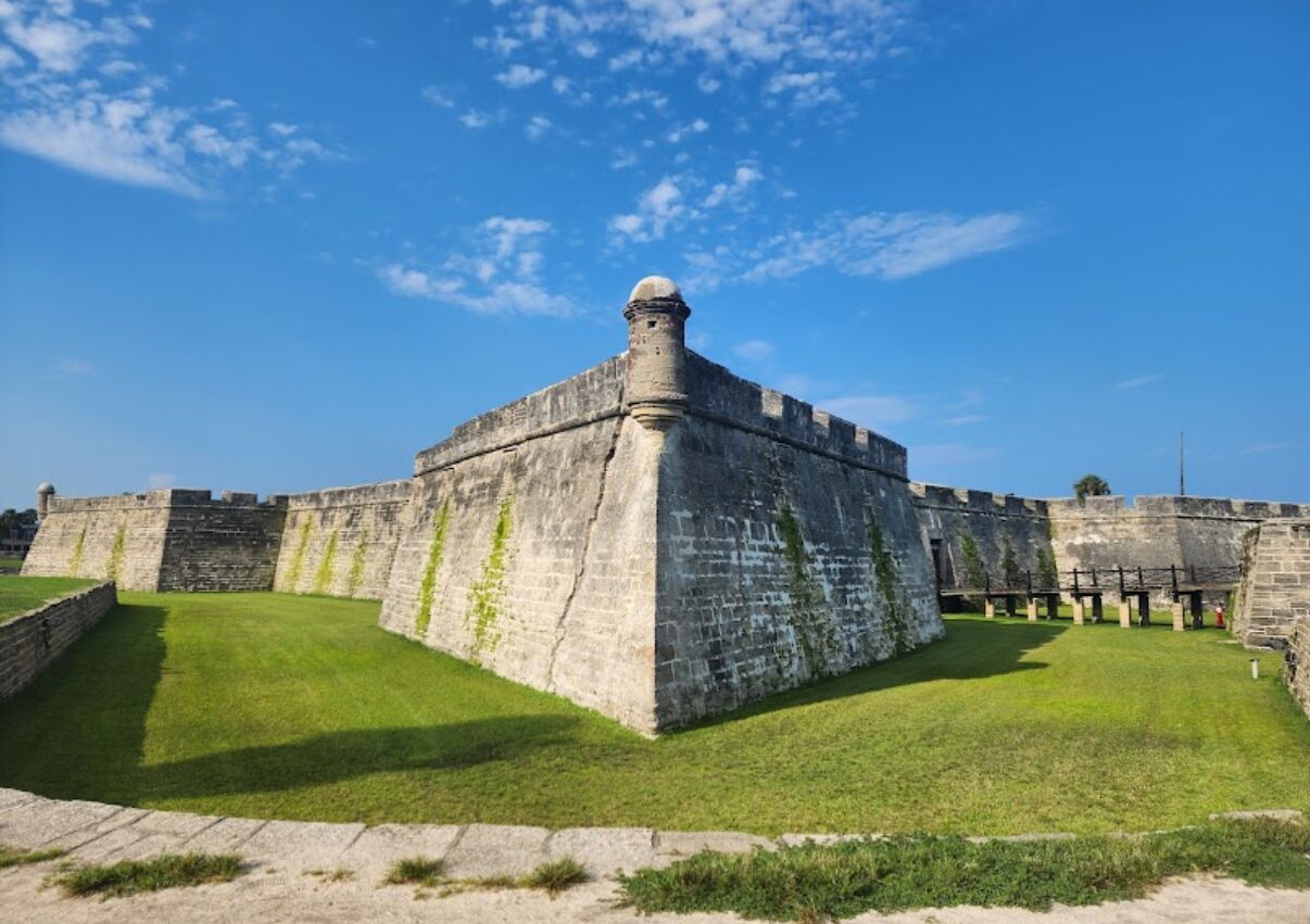 A large, historic stone fort with a central tower, surrounded by a well-maintained grassy area.