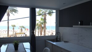 Eine Küche mit Blick auf den Strand, ein Essbereich mit Tisch und Stühlen sowie ein Blumentopf.