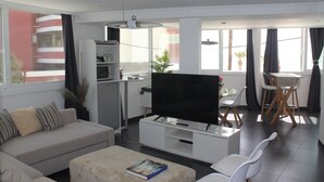 Ein modernes Wohnzimmer mit einer Couch, einem Couchtisch, einem Fernseher und einem Essbereich mit Stühlen und einem Tisch.