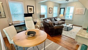 A spacious living room with a wooden dining table, white chairs, a leather sofa, and a staircase leading to another level. - Spring Special 2026!  COMFY URBAN RETREAT, PET FRIENDLY! 30+ nt min✨🌙 (Houston)