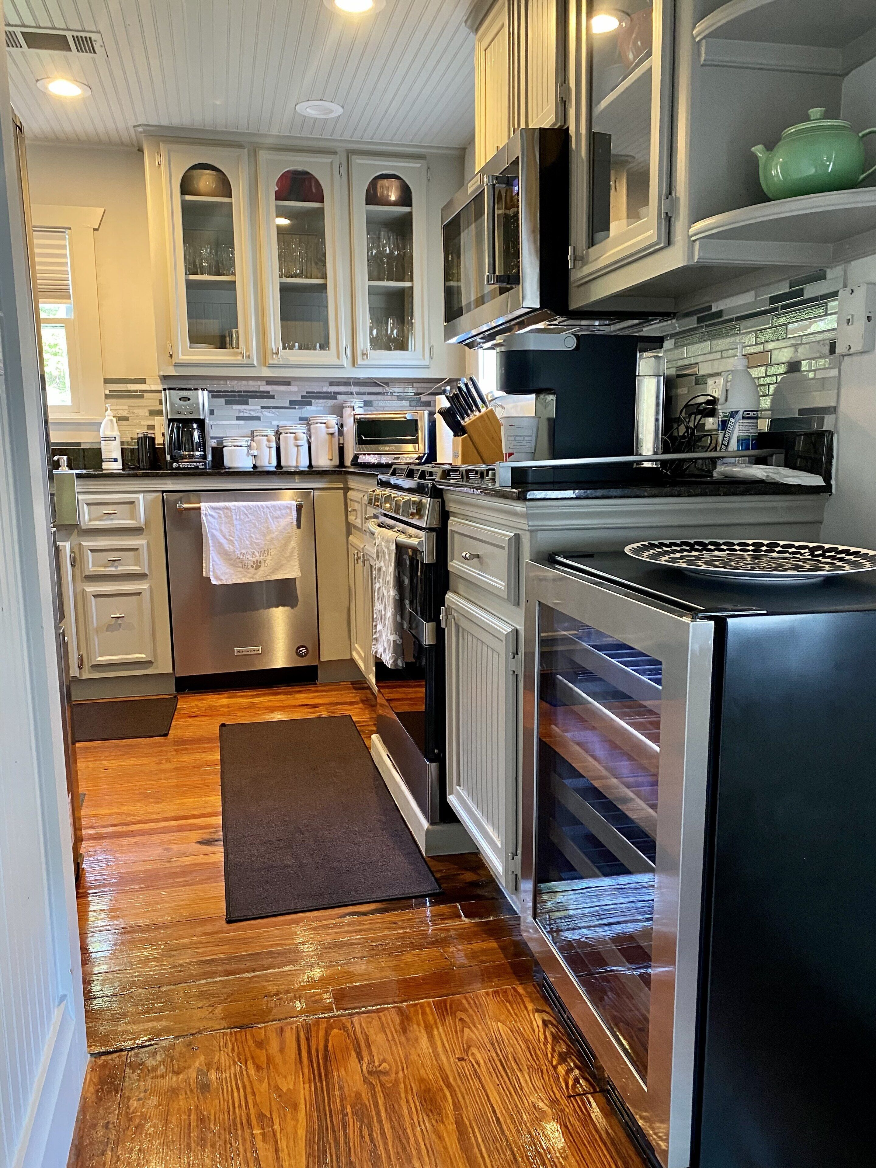 A modern kitchen with stainless steel appliances, wooden flooring, and white cabinetry.