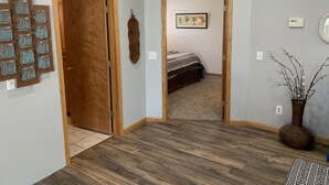 A room with a wooden floor, a bed with a striped blanket, a wall-mounted picture, a decorative wall piece, and a vase with branches. - Lakefront Home/Amazing Lake View/Pomme Paradise #2 (Pittsburg)