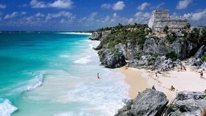 A beach with clear turquoise waters, a sandy shore, and a large ancient stone structure on a cliff. - Jungle vibe,  with  Sea side breezes , EXPERIENCE THE MAYAN RIVIERA  (Akumal)
