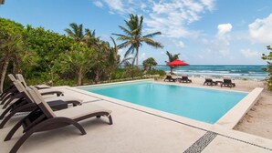 A poolside area with lounge chairs and a red umbrella, overlooking the ocean. - Jungle vibe,  with  Sea side breezes , EXPERIENCE THE MAYAN RIVIERA  (Akumal)