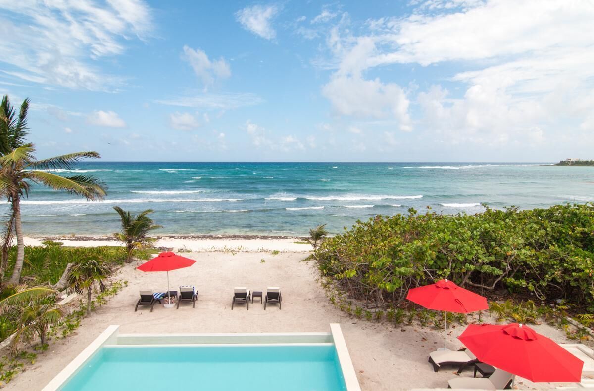 A poolside view with a clear ocean view, lounge chairs, and red umbrellas.