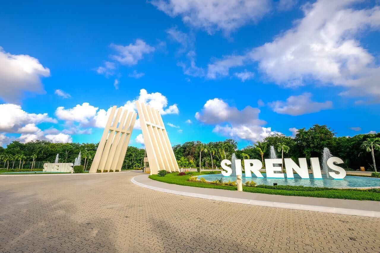 A modern architectural structure with the word "SIRENIS" prominently displayed, surrounded by a landscaped area with a fountain and greenery.