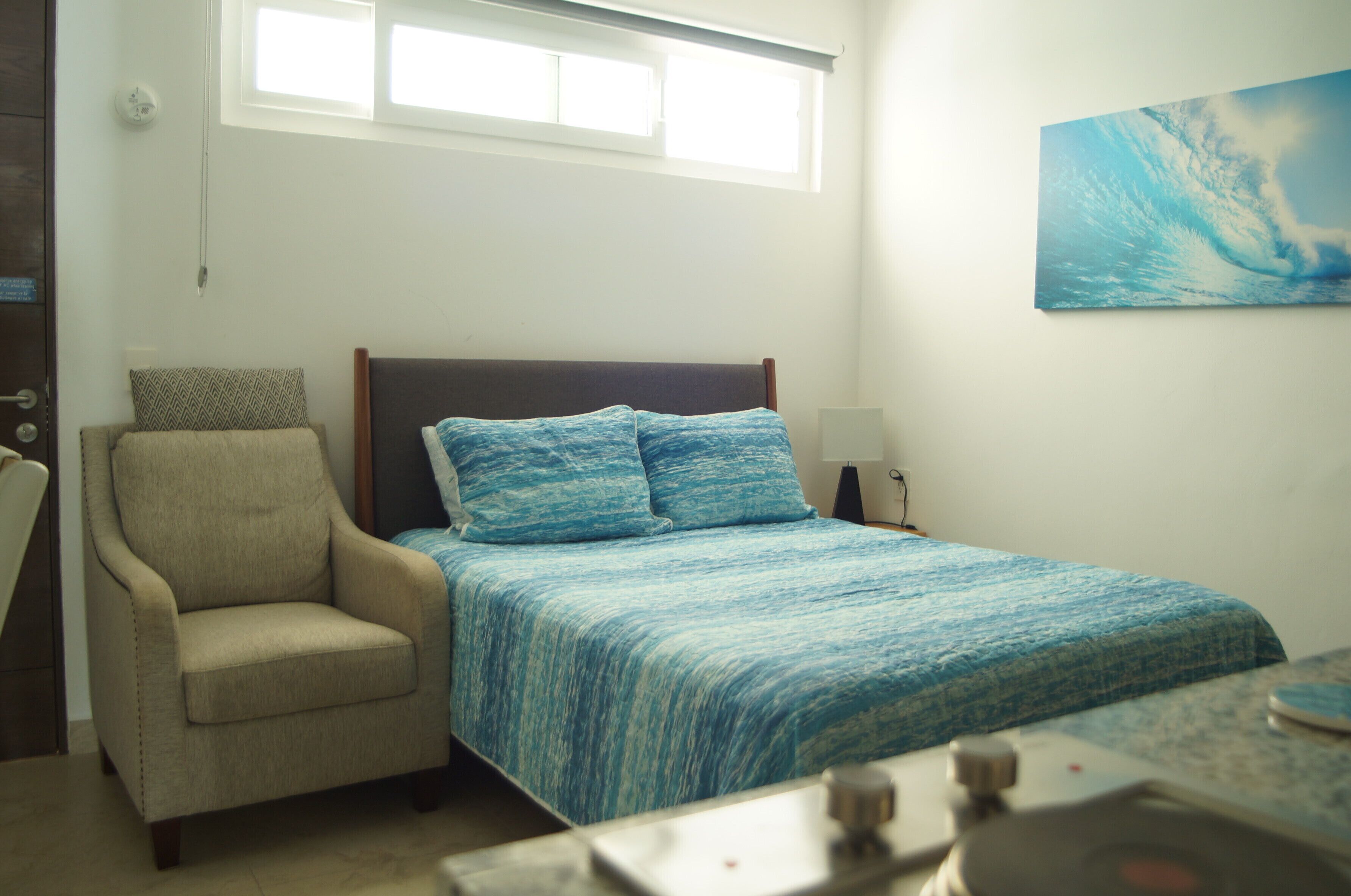A bedroom with a bed, a chair, a desk, and a window.